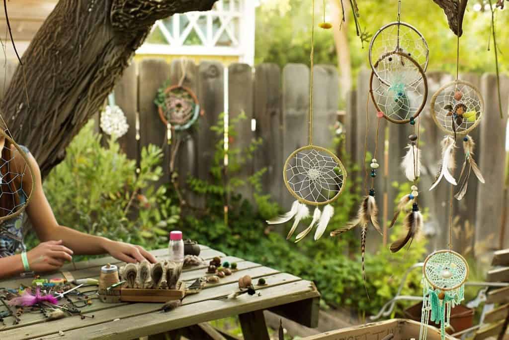 Making nature-inspired dream catchers with twine, feathers, and beads in a garden setting.